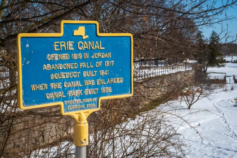 A commemorative plaque documents the history of the Erie Canal: Opened in 1819, abandoned fall of 1917, an extra aqueduct built in 1841 to expand the canal, and a canal park built in 1932.